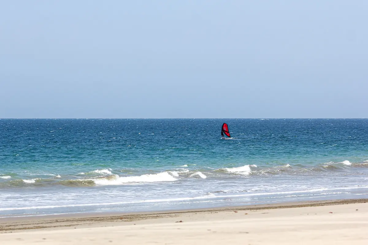 Distant view of a woman wingfoiling on the ocean seen from a wide empty beach at a women's wingfoil camp in Peru.