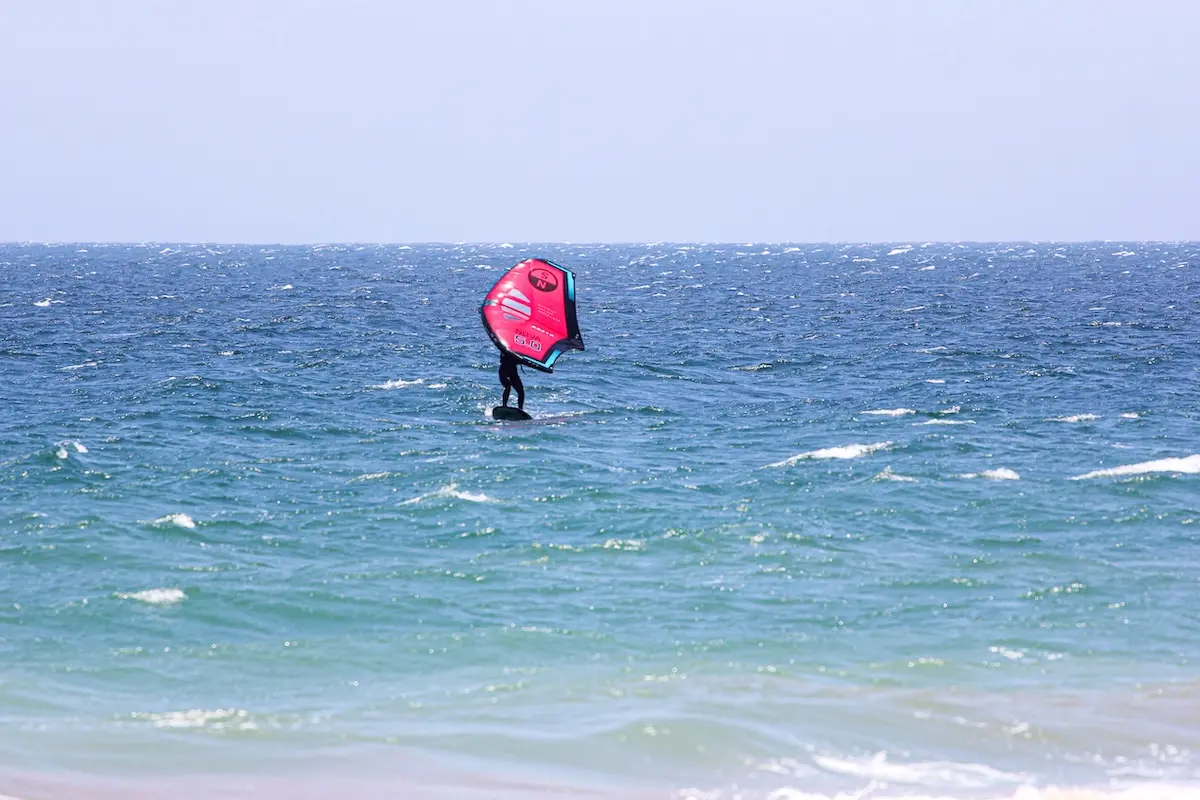 Woman wingfoiling on a foil board with a red North wing on choppy blue ocean waters at a women's wingfoil camp in Peru.