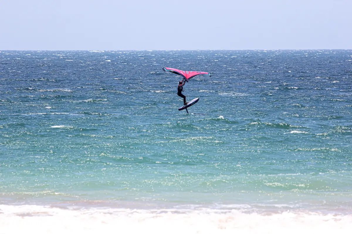 Woman launching high in the air on a wingfoil board with a red wing at a women's wingfoil camp in Peru.