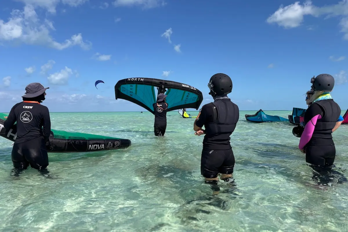 Kite Sisters crew member demonstrating North Nova wing handling technique to two women students in the water during a women's wingfoil retreat in Belize.