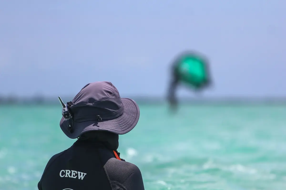 Kite Sisters crew member seen from behind watching a wingfoiler on turquoise Belize waters during a women's wingfoil retreat in Belize.