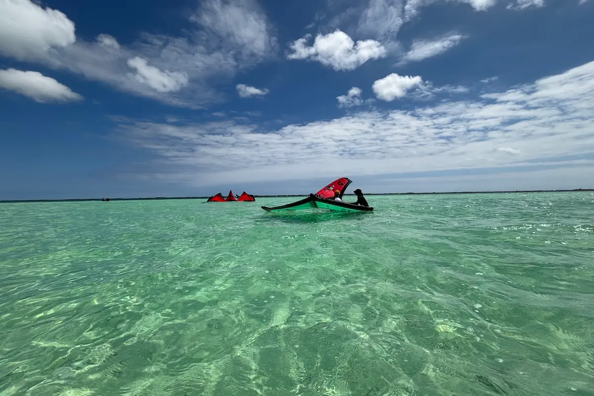Red wingfoil wings and a green boat floating on crystal clear shallow water under a blue sky during a women's wingfoil retreat in Belize.