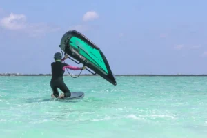 Woman kneeling on a North foil board holding a green North Nova wing on turquoise water during a women's wingfoil retreat in Belize.